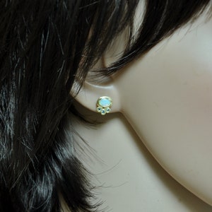 Op de afbeelding: Gouden oorbel studs met een witte opaal edelsteen en kleinere blauwe edelstenen.