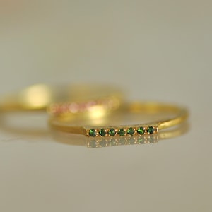 May include: A gold band ring with a row of small green gemstones.