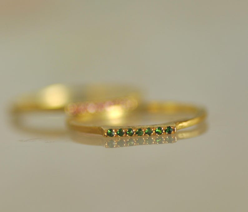 May include: A gold band ring with a row of small green gemstones.