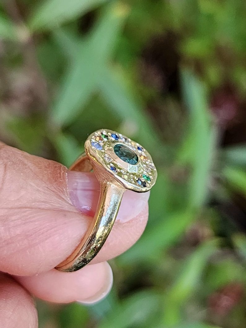 K&ouml;nnte beinhalten: Ein goldener Ring mit einem gro&szlig;en gr&uuml;nen Edelstein, der von kleineren bunten Edelsteinen umgeben ist.