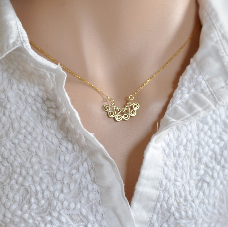 Puede incluir: Un collar de cadena de oro con un delicado colgante que presenta una serie de bucles interconectados.