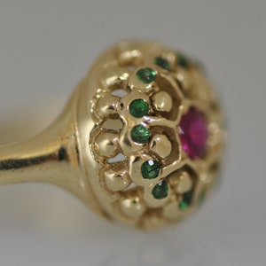 May include: A gold ring with a red ruby and green emeralds set in a delicate, intricate design.