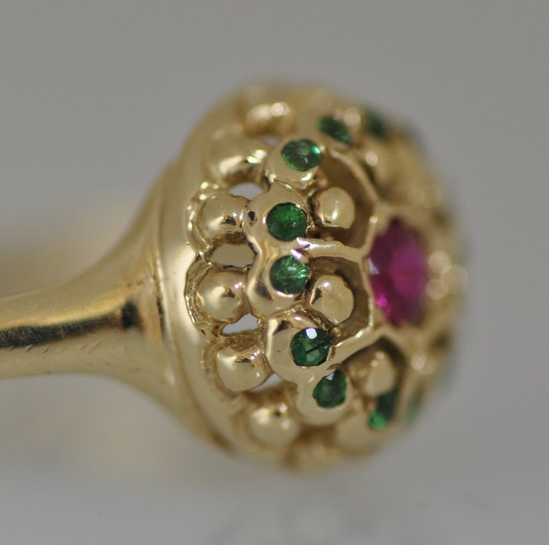 May include: A gold ring with a red ruby and green emeralds set in a delicate, intricate design.