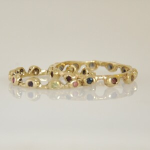 May include: Two gold rings with a textured design and colorful gemstones. The rings are stacked on top of each other.