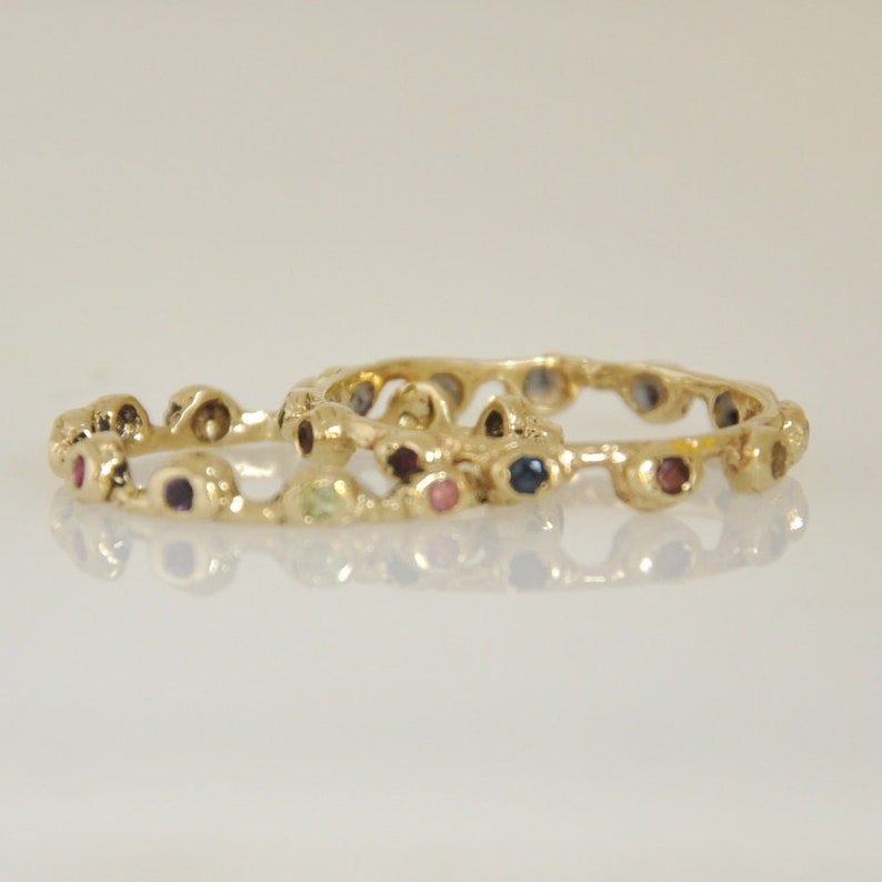 May include: Two gold rings with a textured design and colorful gemstones. The rings are stacked on top of each other.