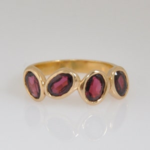 Puede incluir: Un anillo de banda de oro con cuatro piedras preciosas ovaladas de color rojo oscuro.