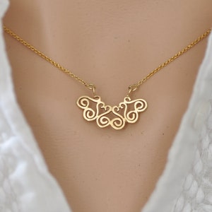 Puede incluir: Un collar de oro con un delicado y complejo colgante que presenta un patr&oacute;n repetitivo de espirales y bucles. El colgante tiene la forma de un abanico o una mariposa.