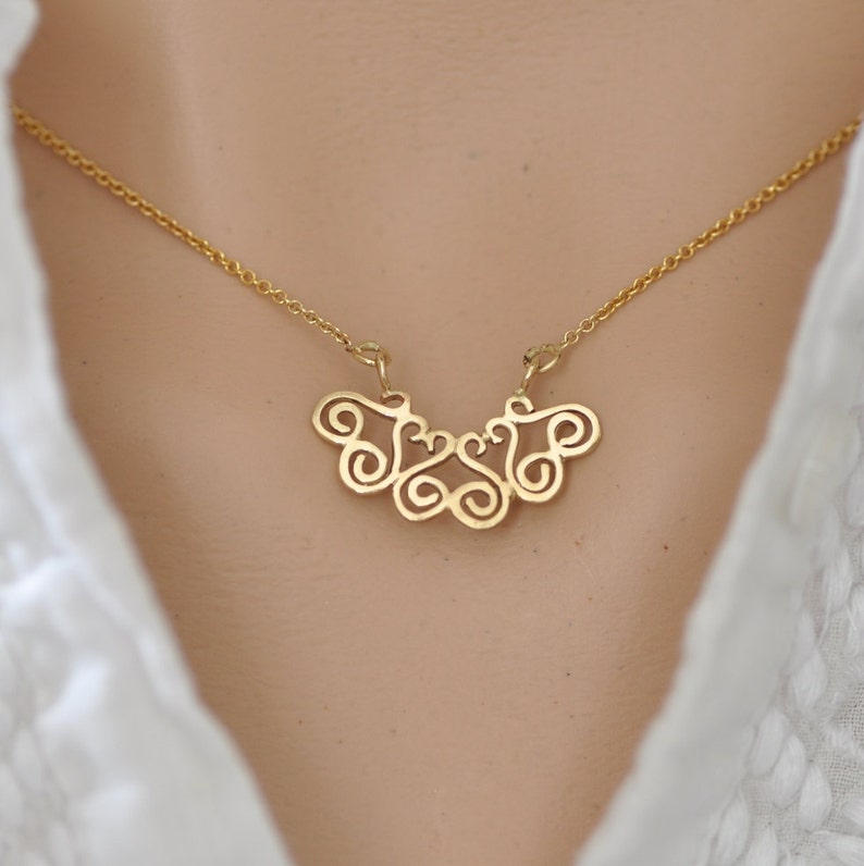 Puede incluir: Un collar de oro con un delicado y complejo colgante que presenta un patr&oacute;n repetitivo de espirales y bucles. El colgante tiene la forma de un abanico o una mariposa.