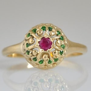 May include: A gold ring with a red ruby gemstone surrounded by green gemstones in a filigree design.