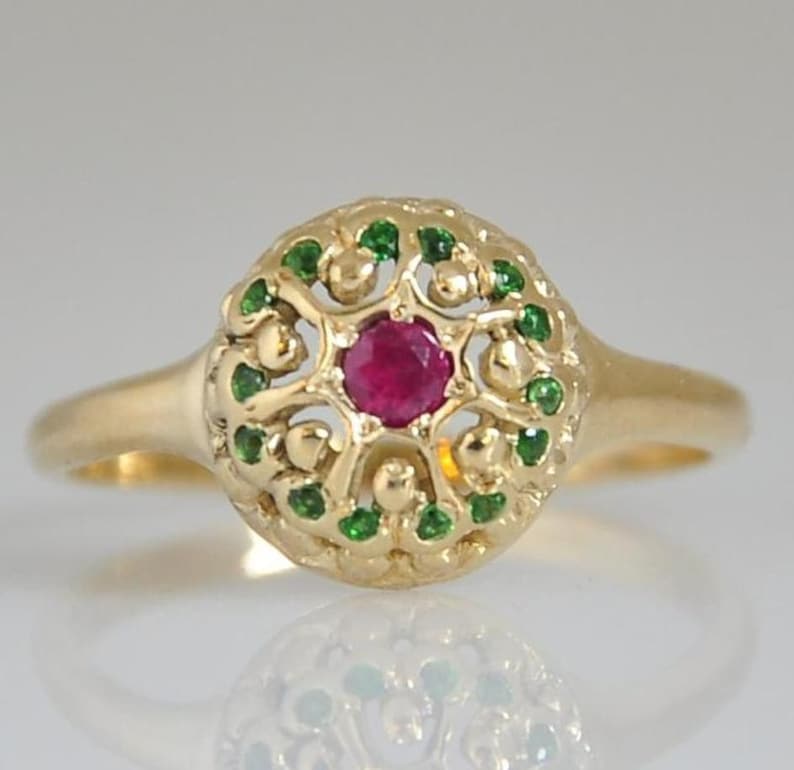 May include: A gold ring with a red ruby gemstone surrounded by green gemstones in a filigree design.