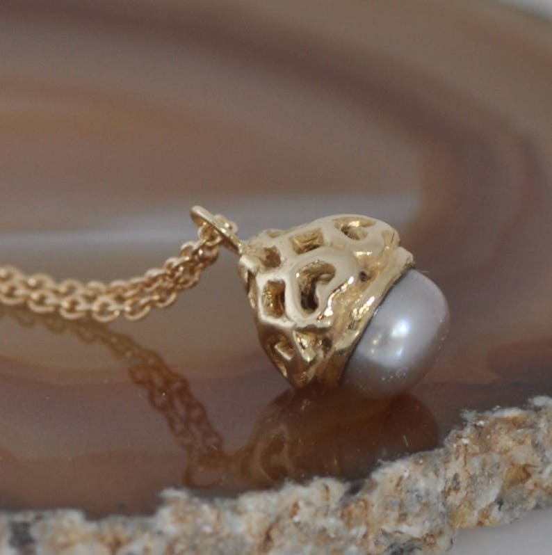 May include: A gold necklace with a delicate chain and a pendant featuring a pearl encased in a gold cage design.