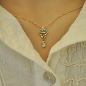 May include: A gold chain necklace with a pendant featuring a blue oval gemstone surrounded by smaller blue gemstones and a teardrop-shaped opal.