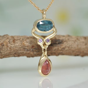May include: Gold pendant necklace with a blue oval gemstone, two small purple gemstones, and a teardrop-shaped red gemstone.