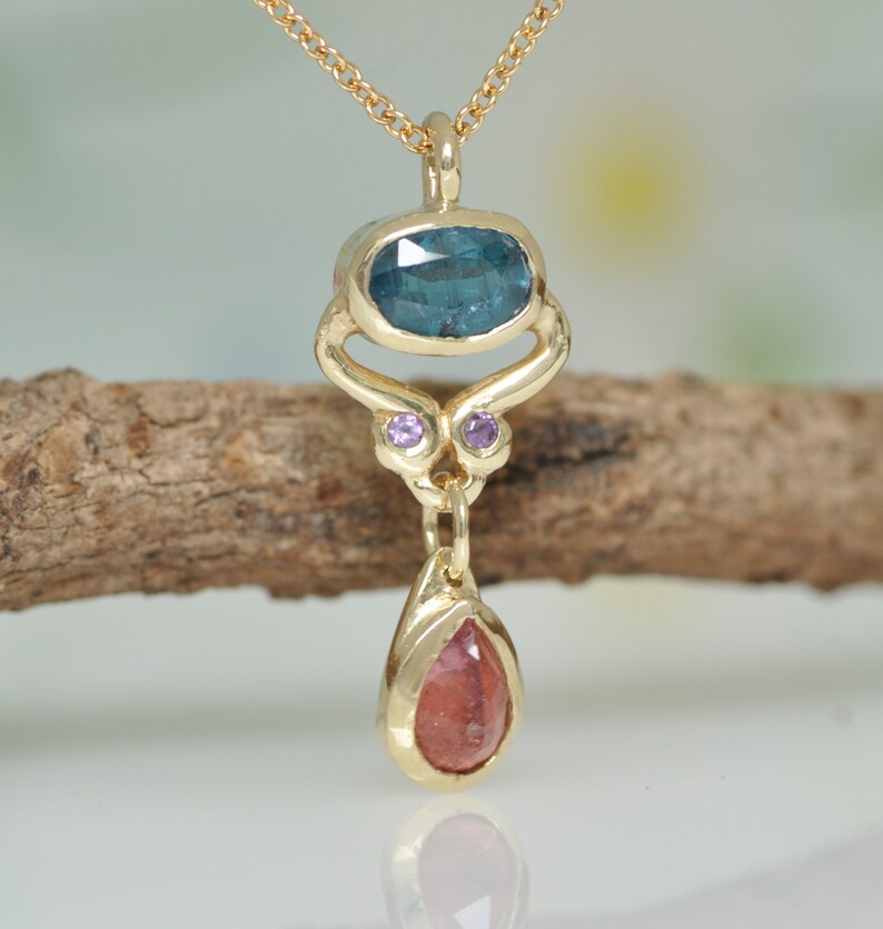 May include: Gold pendant necklace with a blue oval gemstone, two small purple gemstones, and a teardrop-shaped red gemstone.