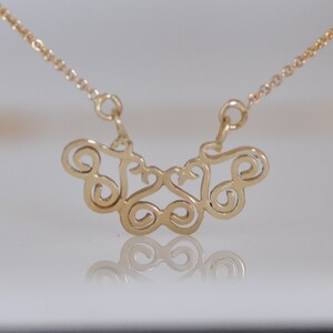 Puede incluir: Un collar de cadena de oro con un delicado y complejo colgante hecho de bucles en espiral interconectados. El colgante tiene la forma de una mariposa.