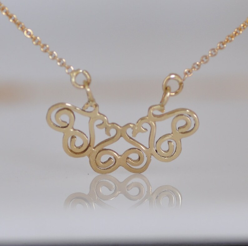 Puede incluir: Un collar de cadena de oro con un delicado y complejo colgante hecho de bucles en espiral interconectados. El colgante tiene la forma de una mariposa.
