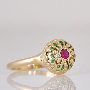May include: A gold ring with a red ruby gemstone surrounded by green emeralds in a filigree design.