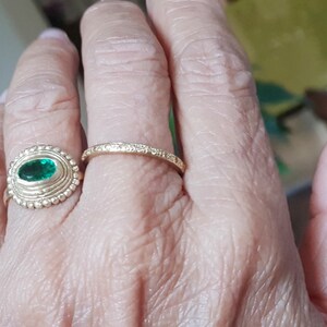 May include: A gold ring with a green oval gemstone set in a textured bezel. A second, thinner gold band is worn on the same finger.