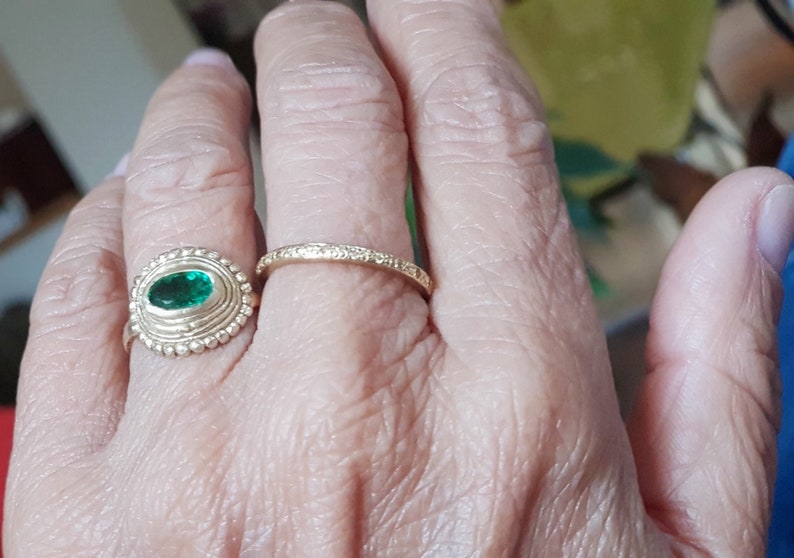May include: A gold ring with a green oval gemstone set in a textured bezel. A second, thinner gold band is worn on the same finger.