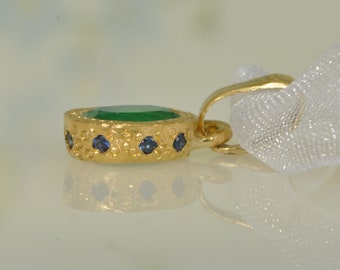 May include: A gold pendant with a green gemstone surrounded by small blue gemstones.