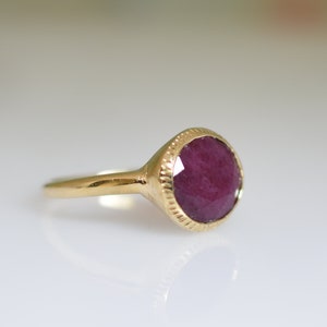 May include: A gold ring with a deep red gemstone set in a textured bezel.