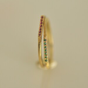 May include: Two gold rings with a single row of small red and green gemstones.