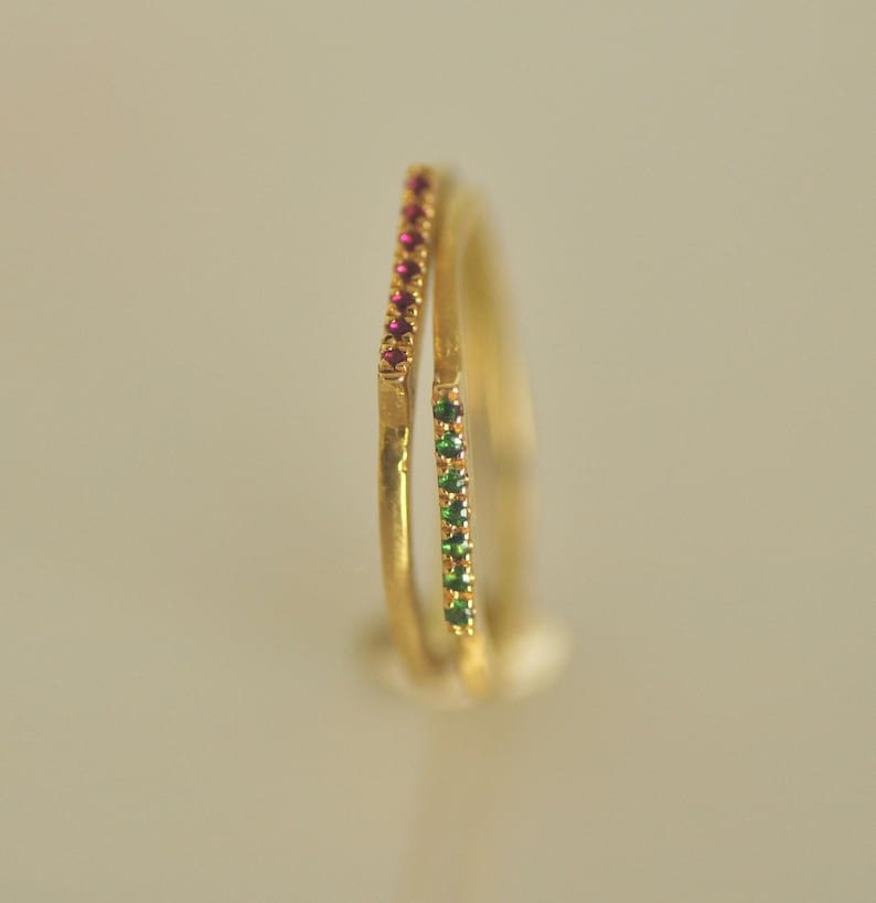 May include: Two gold rings with a single row of small red and green gemstones.