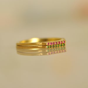 May include: A gold band ring with a row of pink and green gemstones.