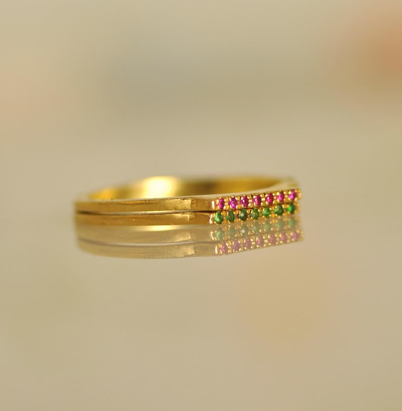 May include: A gold band ring with a row of pink and green gemstones.