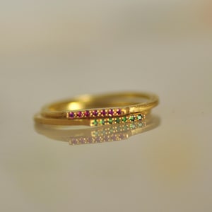 May include: Two thin gold bands with a row of small pink and green gemstones set into the metal.