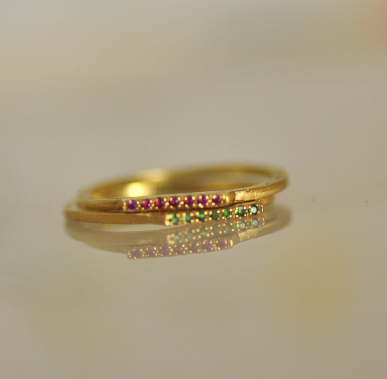 May include: Two thin gold bands with a row of small pink and green gemstones set into the metal.