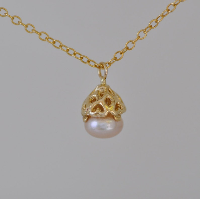 May include: A delicate gold necklace with a heart-shaped cage pendant that holds a single pearl.