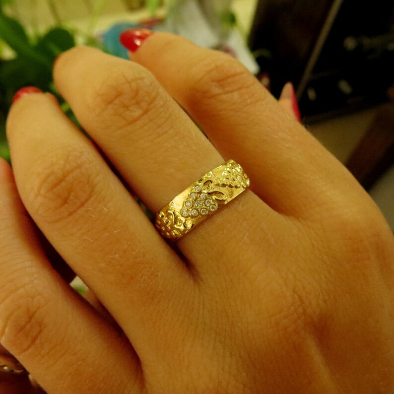 Puede incluir: Un anillo de banda de oro con un dise&ntilde;o floral y peque&ntilde;as piedras transparentes engastadas en la banda.