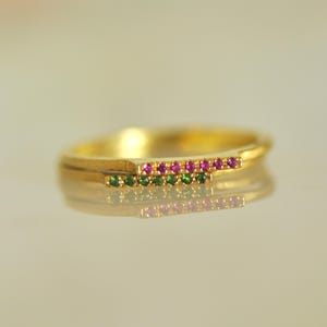 May include: A gold ring with two rows of small gemstones. The top row is pink and the bottom row is green.