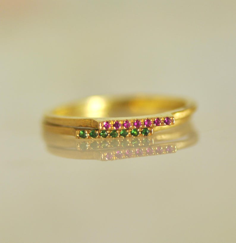 May include: A gold ring with two rows of small gemstones. The top row is pink and the bottom row is green.