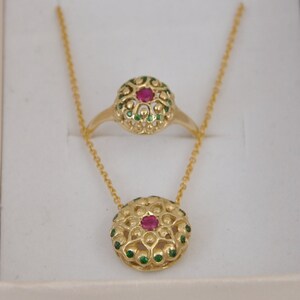 May include: A gold necklace and ring set with a red gemstone surrounded by green gemstones.