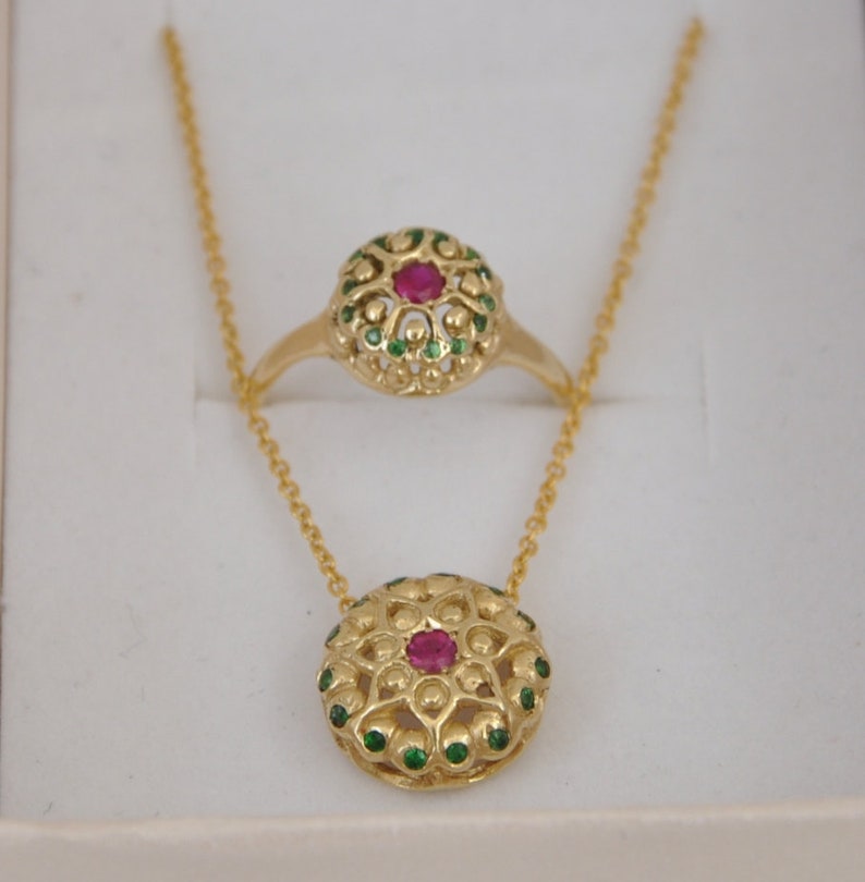 May include: A gold necklace and ring set with a red gemstone surrounded by green gemstones.
