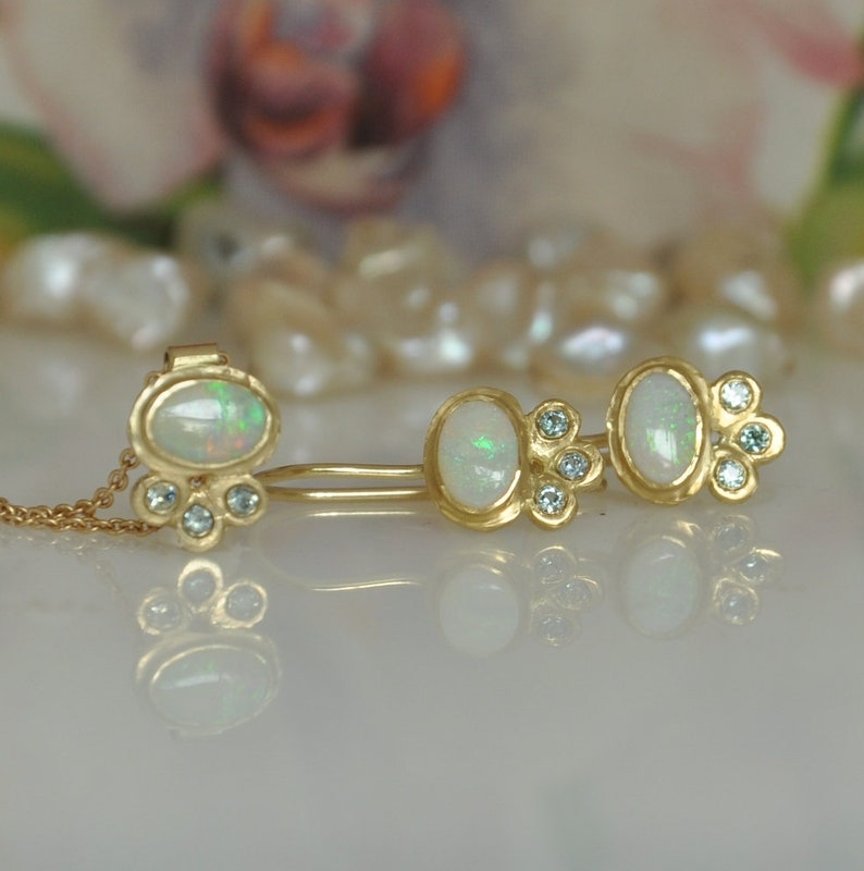 Op de afbeelding: Een paar gouden oorbellen met opaal edelstenen en kleine blauwe diamanten. De oorbellen zijn gezet in een delicaat, bloemig ontwerp.