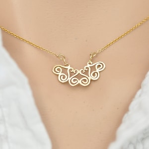 Puede incluir: Un collar de oro con un delicado y complejo colgante que presenta un dise&ntilde;o abstracto en espiral.