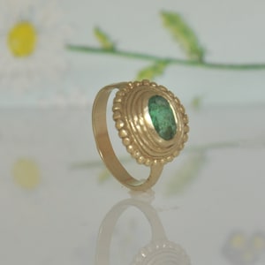 May include: A gold ring with a green gemstone set in a bezel setting. The ring has a decorative band with a beaded design.