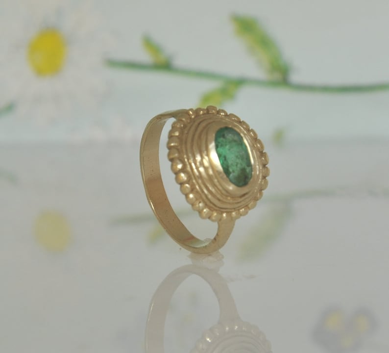 May include: A gold ring with a green gemstone set in a bezel setting. The ring has a decorative band with a beaded design.