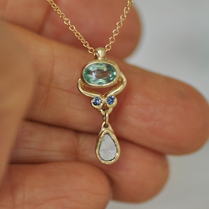 May include: A gold necklace with a pendant featuring a light blue oval gemstone, two smaller blue gemstones, and a teardrop-shaped white gemstone.