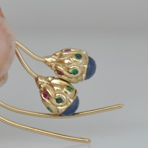 May include: A pair of gold earrings with blue, green, and red gemstones. The earrings are shaped like teardrops and have a delicate, ornate design.