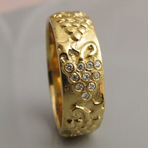 Puede incluir: Un anillo de banda de oro con un dise&ntilde;o texturizado de una vid y un racimo de peque&ntilde;os diamantes.