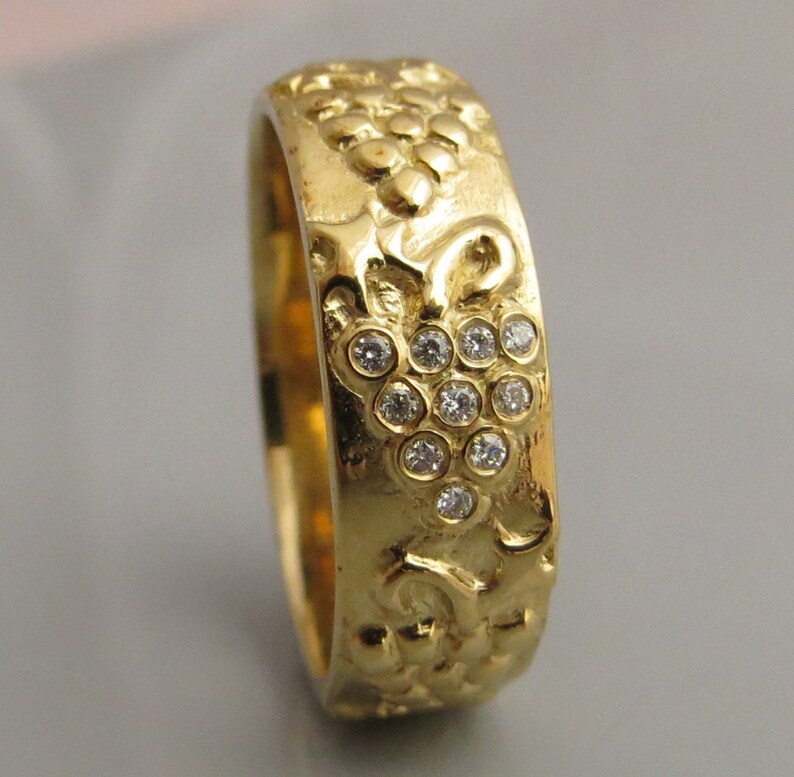 Puede incluir: Un anillo de banda de oro con un dise&ntilde;o texturizado de una vid y un racimo de peque&ntilde;os diamantes.