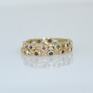 May include: A gold ring with a wavy design and colorful gemstones. The ring is made of two bands, each with a row of small gemstones.
