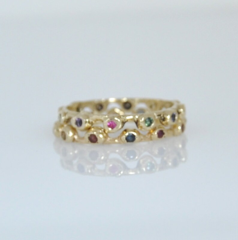 May include: A gold ring with a wavy design and colorful gemstones. The ring is made of two bands, each with a row of small gemstones.