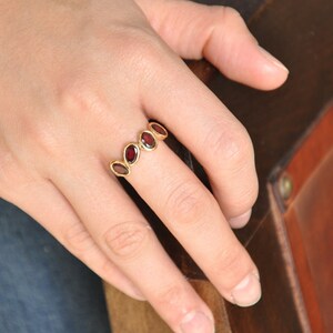 Puede incluir: Un anillo de oro con una banda de piedras preciosas rojas ovaladas.