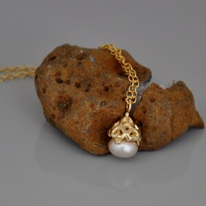 May include: A gold chain necklace with a delicate pearl pendant. The pendant is a small, intricate design with a pearl in the center.