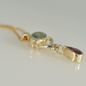 May include: A gold pendant necklace with a light blue oval gemstone and a teardrop-shaped pink gemstone.